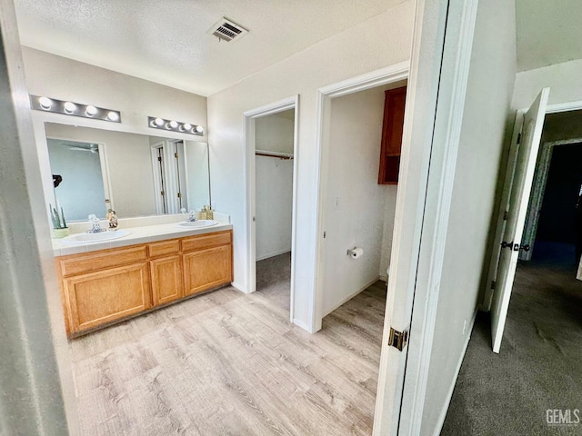 bathroom with double vanity, wood finished floors, a sink, and visible vents