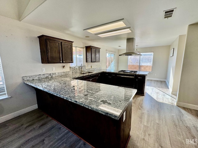 kitchen featuring a peninsula, a sink, visible vents, light stone countertops, and island exhaust hood