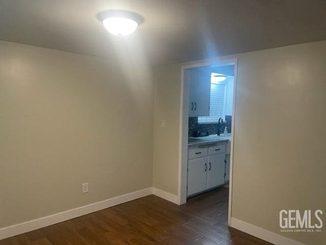 empty room featuring dark wood-style floors, baseboards, and a sink