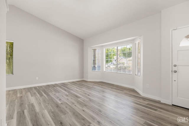 foyer entrance featuring light wood-style floors, vaulted ceiling, and baseboards