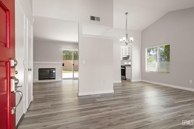 entrance foyer with lofted ceiling, wood finished floors, visible vents, baseboards, and a brick fireplace