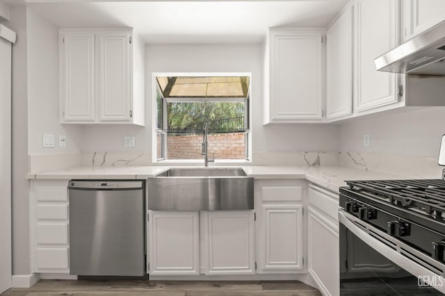 kitchen with appliances with stainless steel finishes, white cabinetry, a sink, light stone countertops, and under cabinet range hood