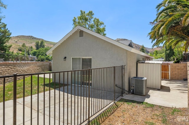 view of property exterior with central AC unit, fence private yard, a mountain view, a gate, and stucco siding