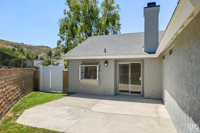 exterior space with a mountain view, fence, stucco siding, a chimney, and a patio area