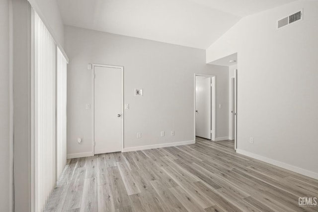 unfurnished room featuring vaulted ceiling, light wood finished floors, visible vents, and baseboards