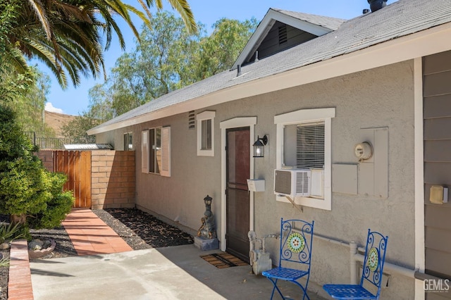 entrance to property featuring roof with shingles, cooling unit, fence, and stucco siding