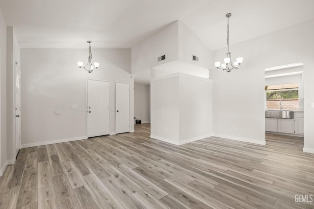 interior space with a chandelier, high vaulted ceiling, light wood finished floors, and visible vents