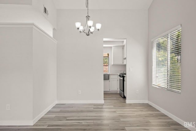 unfurnished dining area featuring visible vents, light wood-style flooring, baseboards, and an inviting chandelier