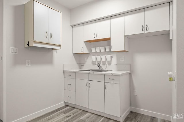 kitchen with light countertops, a sink, white cabinetry, and baseboards