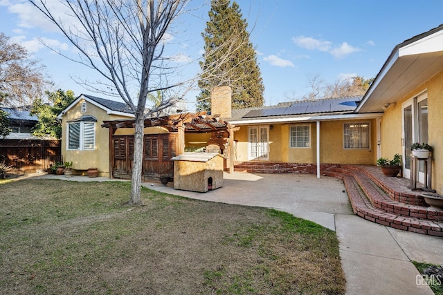 rear view of house with solar panels, a patio, and a lawn