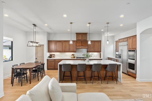 kitchen with stainless steel appliances, a large island, decorative backsplash, brown cabinetry, and light countertops