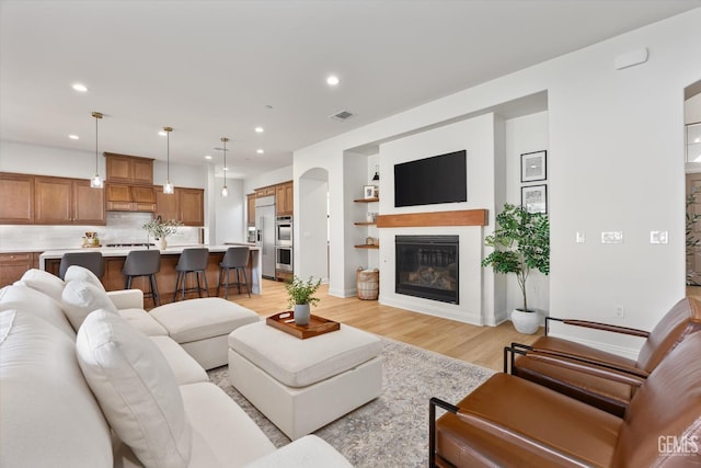 living room with a glass covered fireplace, light wood-style floors, baseboards, visible vents, and recessed lighting