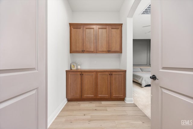 hall featuring arched walkways, light wood-type flooring, visible vents, and baseboards