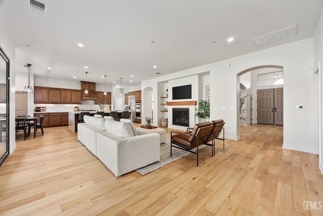 living room featuring light wood finished floors, visible vents, arched walkways, and recessed lighting