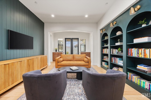 living room featuring recessed lighting, wood walls, french doors, light wood-style flooring, and built in shelves