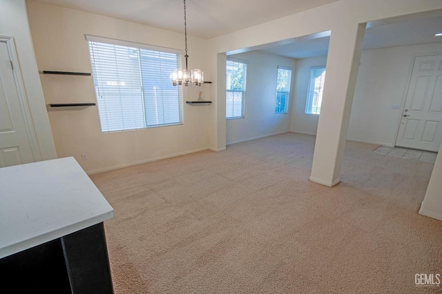 unfurnished dining area with light colored carpet, baseboards, and an inviting chandelier