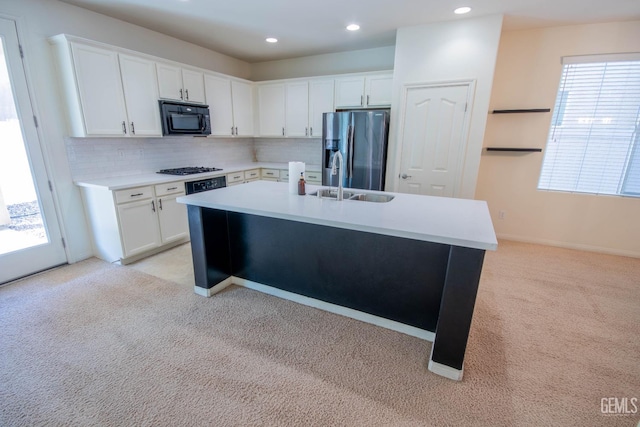 kitchen featuring a center island with sink, white cabinets, light colored carpet, appliances with stainless steel finishes, and light countertops