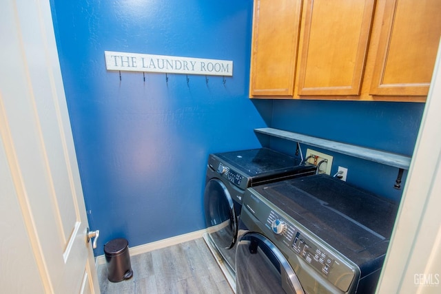 clothes washing area featuring wood finished floors, washing machine and dryer, cabinet space, and baseboards