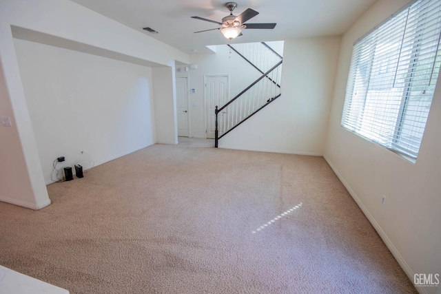 unfurnished living room with light colored carpet, visible vents, baseboards, stairs, and a ceiling fan