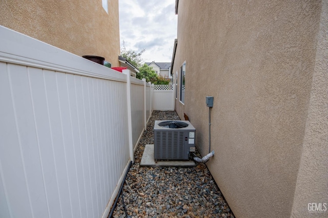 view of side of home with stucco siding, fence, and central AC unit