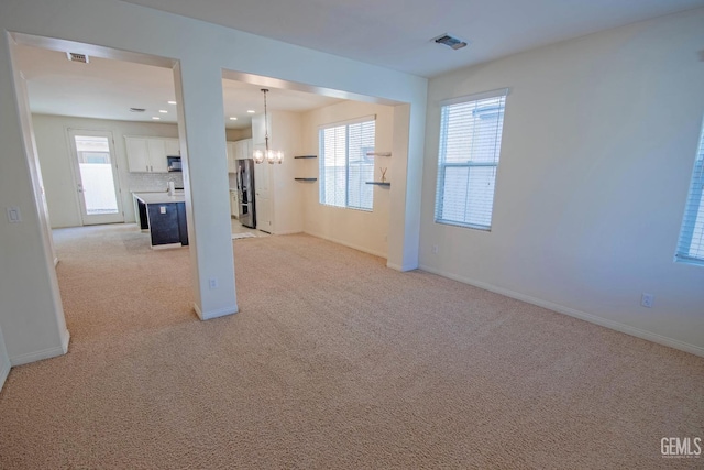 spare room featuring a chandelier, visible vents, and light colored carpet