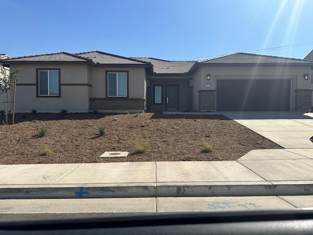 prairie-style home with driveway, an attached garage, a tile roof, and stucco siding