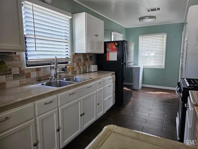 kitchen featuring white cabinetry, sink, stainless steel gas range, black fridge, and decorative backsplash