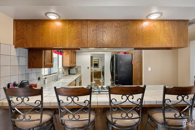 6801 Weldon Ave, Bakersfield, CA 93308 - kitchen with tile countertops, freestanding refrigerator, a breakfast bar, brown cabinets, and a sink