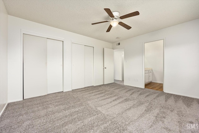 unfurnished bedroom with carpet floors, multiple closets, visible vents, a textured ceiling, and ensuite bath