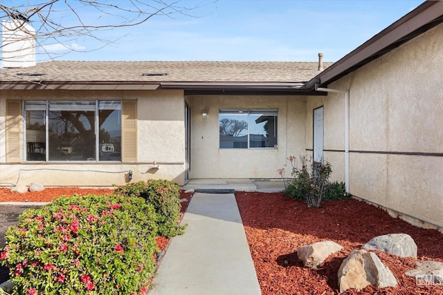 entrance to property featuring roof with shingles and stucco siding