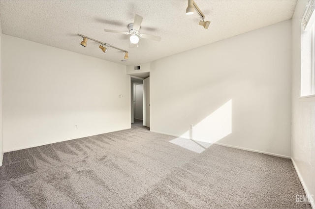 carpeted spare room with rail lighting, visible vents, a ceiling fan, a healthy amount of sunlight, and a textured ceiling