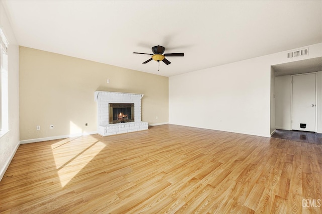 unfurnished living room featuring ceiling fan, visible vents, baseboards, light wood-style floors, and a brick fireplace