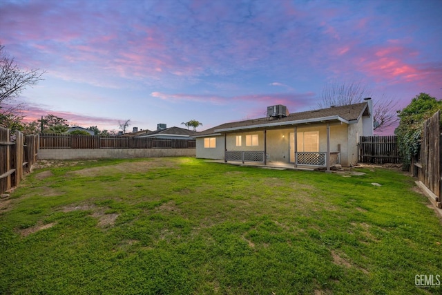 back of property at dusk featuring a fenced backyard, a lawn, and central air condition unit