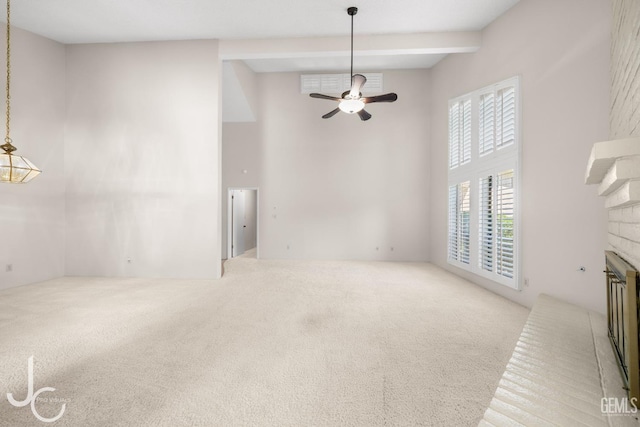 unfurnished living room featuring a brick fireplace, carpet, a towering ceiling, and ceiling fan