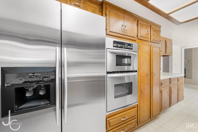 kitchen featuring light countertops, appliances with stainless steel finishes, brown cabinetry, and light tile patterned floors