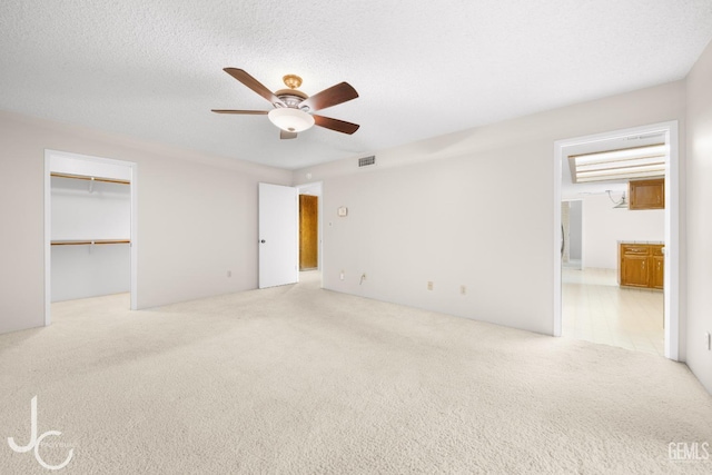 unfurnished bedroom featuring visible vents, ceiling fan, a spacious closet, carpet, and ensuite bath