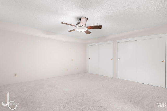 unfurnished bedroom with carpet floors, a textured ceiling, multiple closets, and ceiling fan