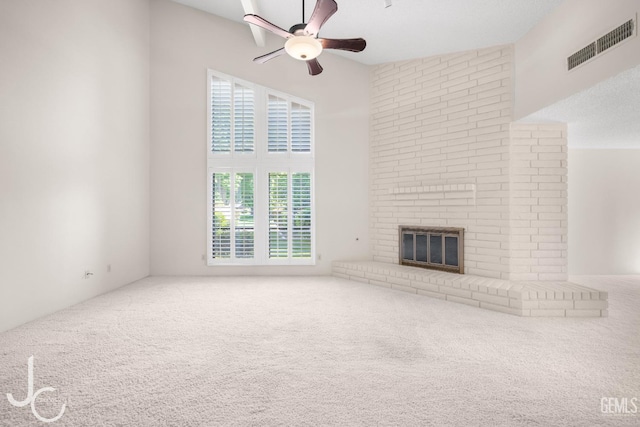 unfurnished living room featuring a ceiling fan, a towering ceiling, visible vents, a fireplace, and carpet floors