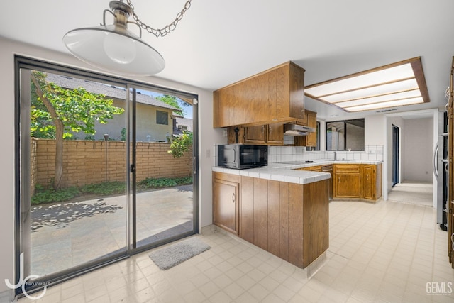 kitchen featuring a sink, brown cabinetry, tile countertops, a peninsula, and black appliances