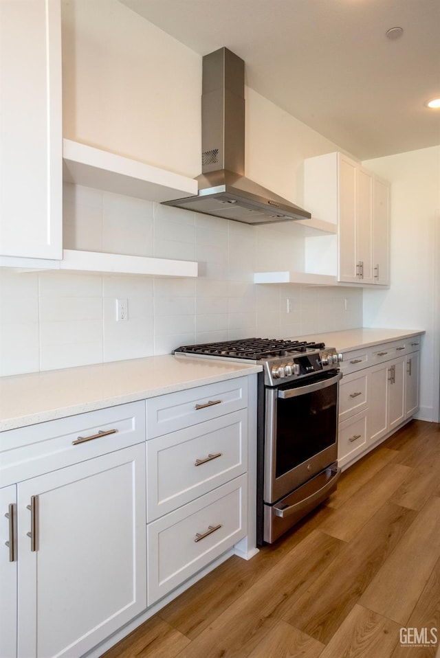 kitchen featuring stainless steel range with gas stovetop, tasteful backsplash, ventilation hood, light hardwood / wood-style floors, and white cabinets