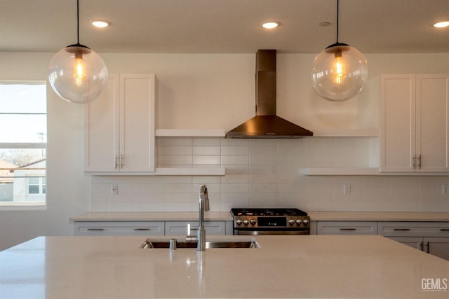 kitchen with decorative light fixtures, stainless steel range oven, sink, and wall chimney range hood