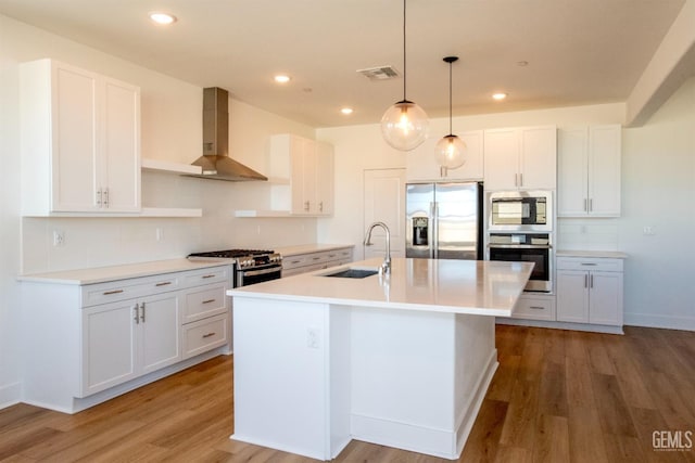 kitchen with white cabinetry, sink, a kitchen island with sink, stainless steel appliances, and wall chimney range hood