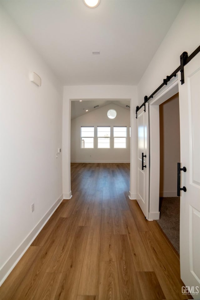 hall featuring lofted ceiling, wood-type flooring, and a barn door