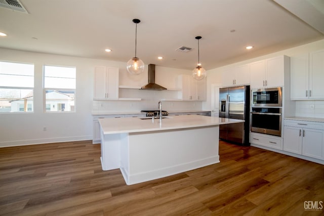 kitchen featuring white cabinets, stainless steel fridge, an island with sink, and wall chimney range hood