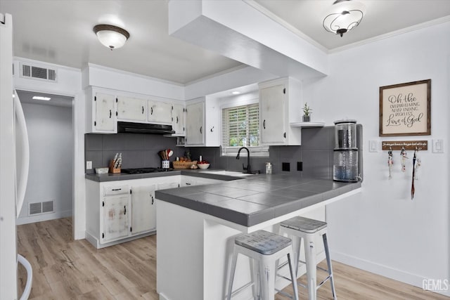 5906 Ronald Way, Bakersfield, CA 93308 - kitchen featuring a peninsula, white cabinetry, light wood-style floors, a kitchen bar, and under cabinet range hood