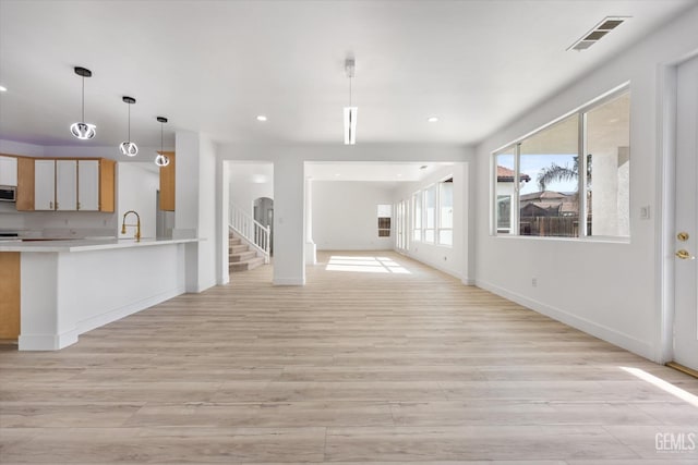 interior space featuring pendant lighting, sink, light hardwood / wood-style floors, kitchen peninsula, and stainless steel appliances