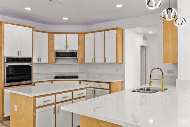 kitchen with sink, appliances with stainless steel finishes, light stone counters, white cabinets, and kitchen peninsula