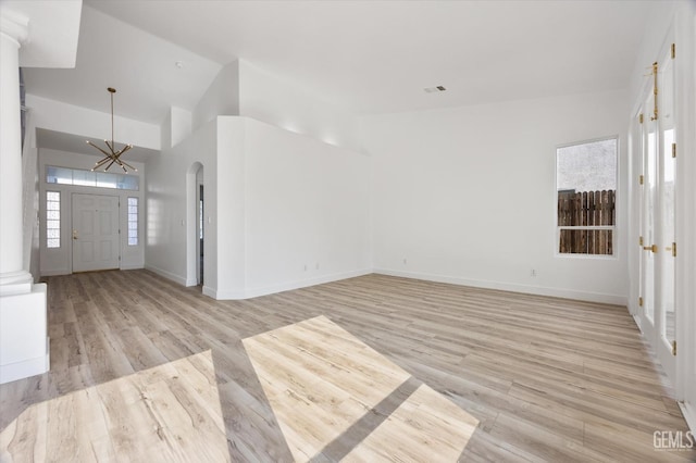 unfurnished living room with high vaulted ceiling, a chandelier, and light hardwood / wood-style floors