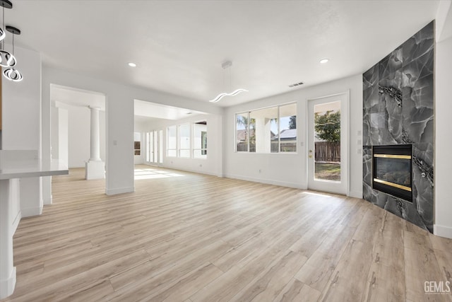 unfurnished living room with a premium fireplace, ornate columns, and light wood-type flooring