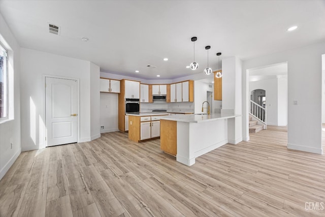 kitchen featuring light hardwood / wood-style floors, hanging light fixtures, oven, and kitchen peninsula